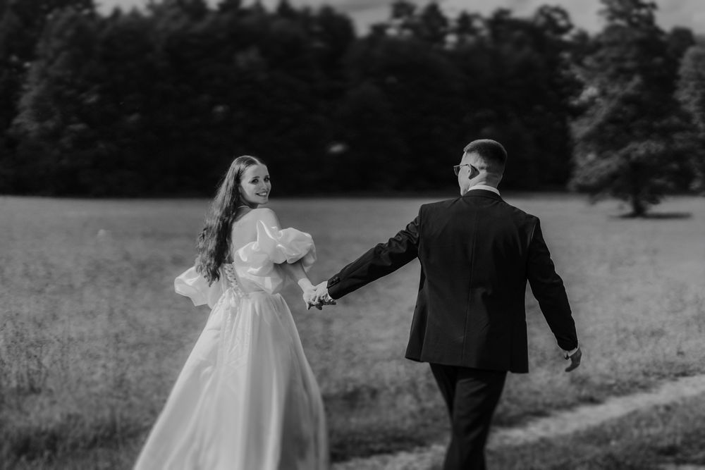 Couple walking hand in hand through a meadow in wedding attire.