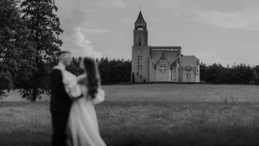 A romantic silhouette of a couple embracing in front of a majestic church with a tall spire in black and white.