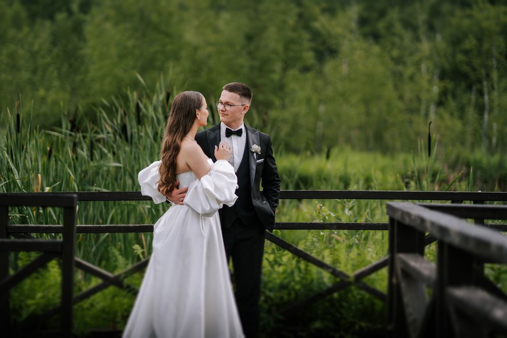 Romantic wedding portrait on rustic bridge with natural backdrop.