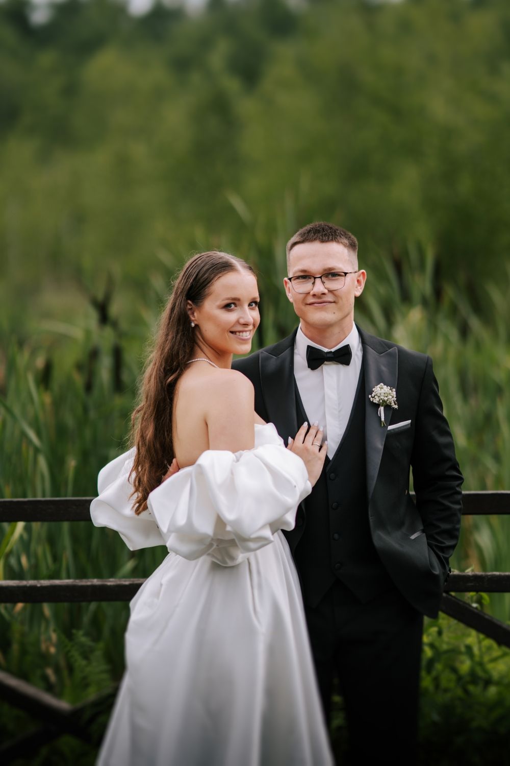 Elegant couple poses on wooden bridge surrounded by lush greenery.