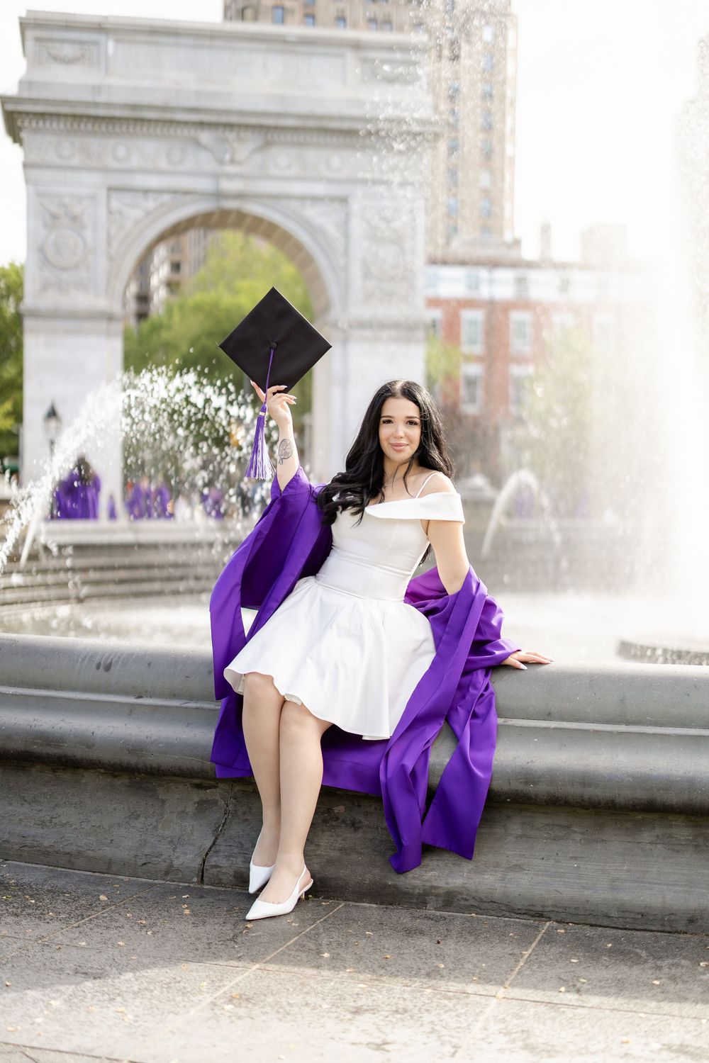 Graduation photos taken near a fountain showing purple academic regalia and white dress.