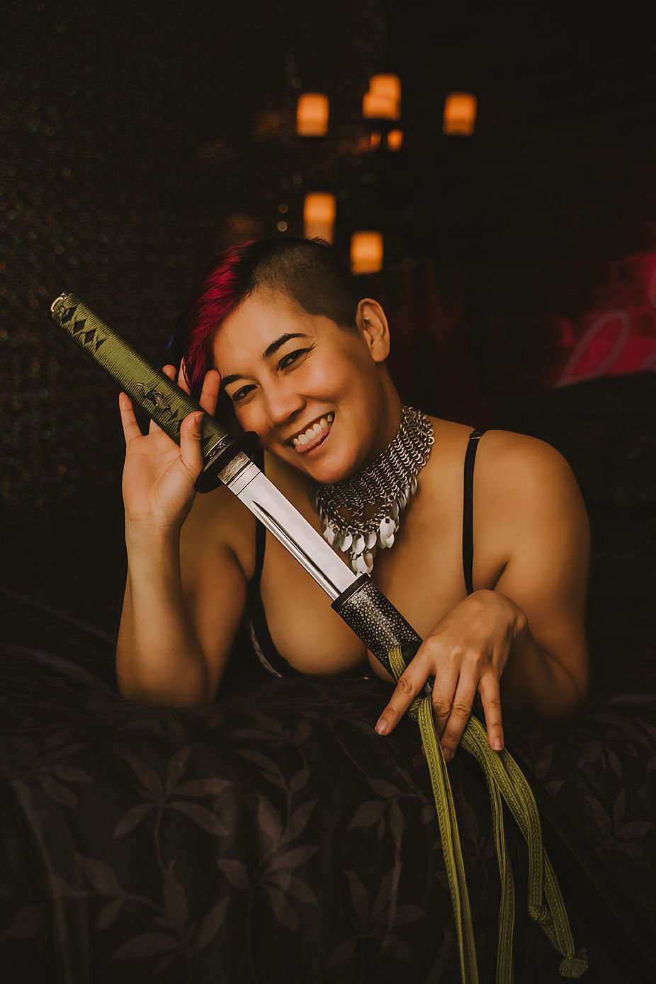 Dramatic portrait with katana sword and silver choker necklace against dark background with glowing lanterns.