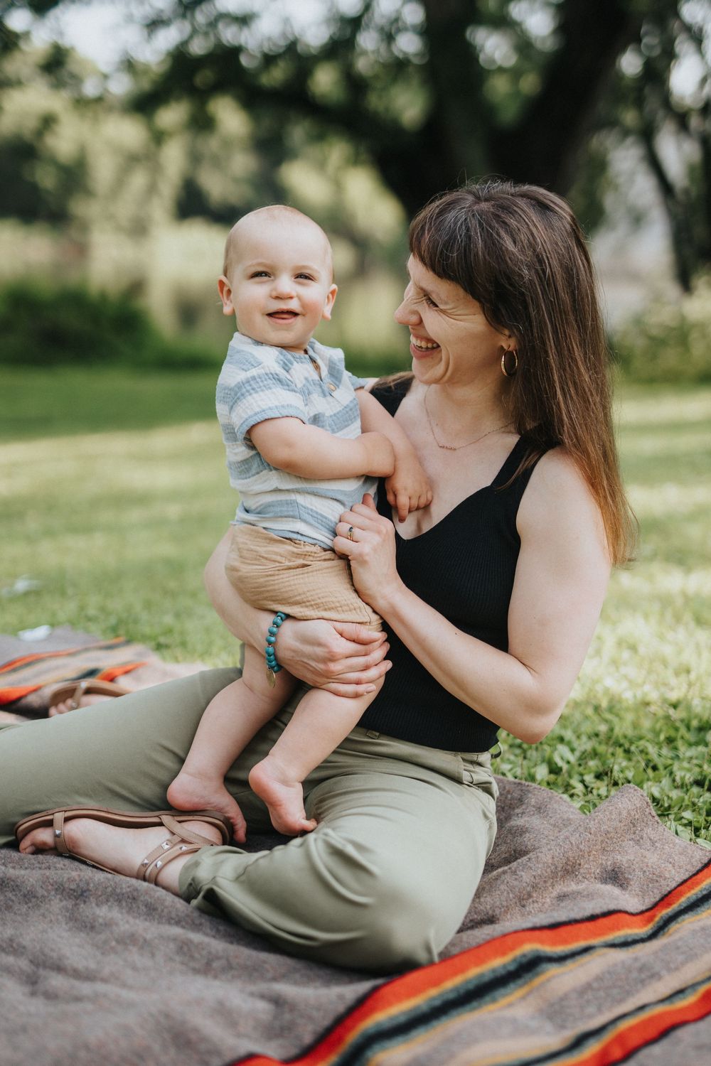 A heartwarming outdoor photo session on a blanket shows tender moments between parent and baby in casual summer attire.