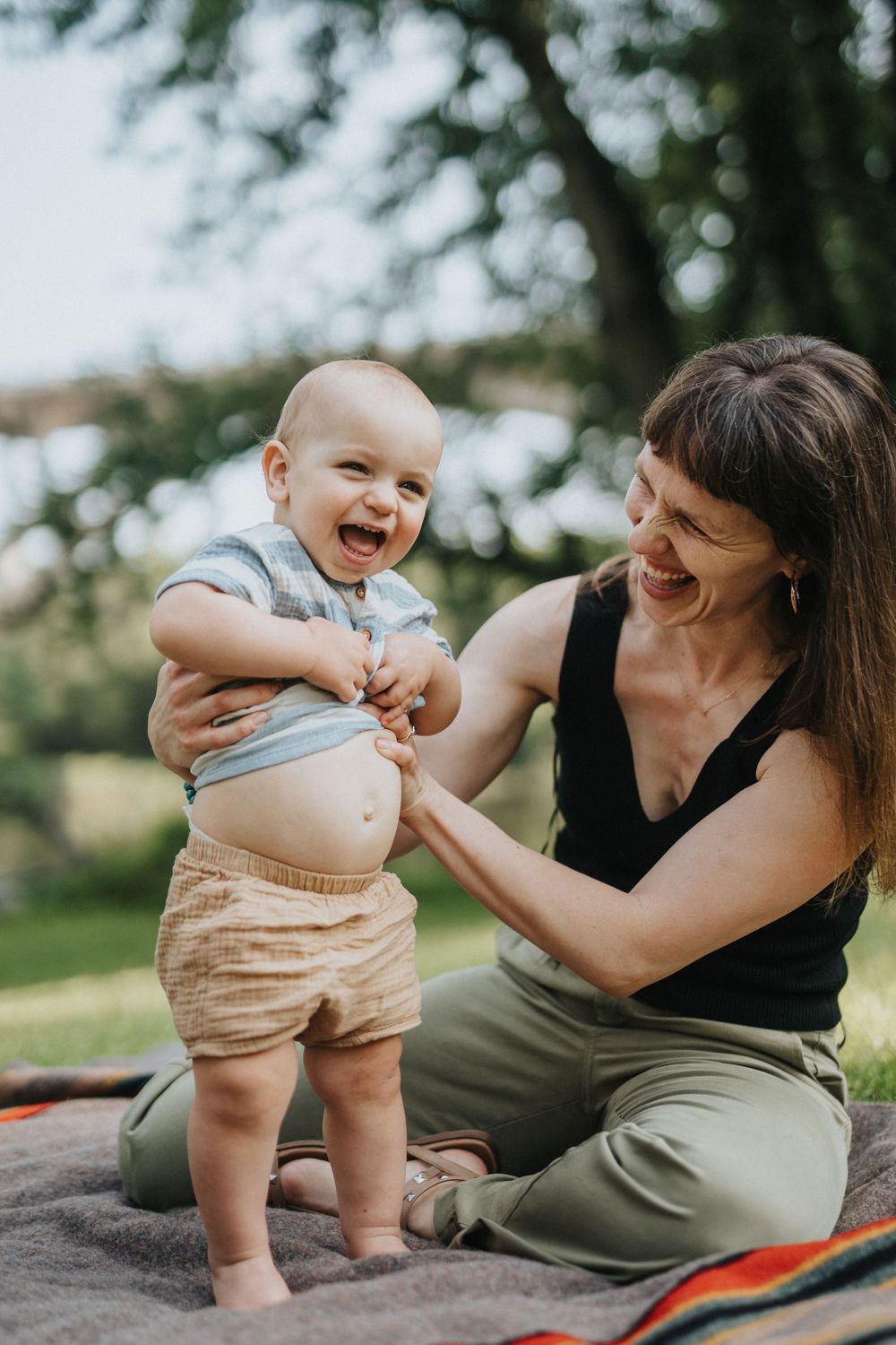 Candid outdoor portraits capture joyful interactions between parent and baby sitting on a picnic blanket in a park.
