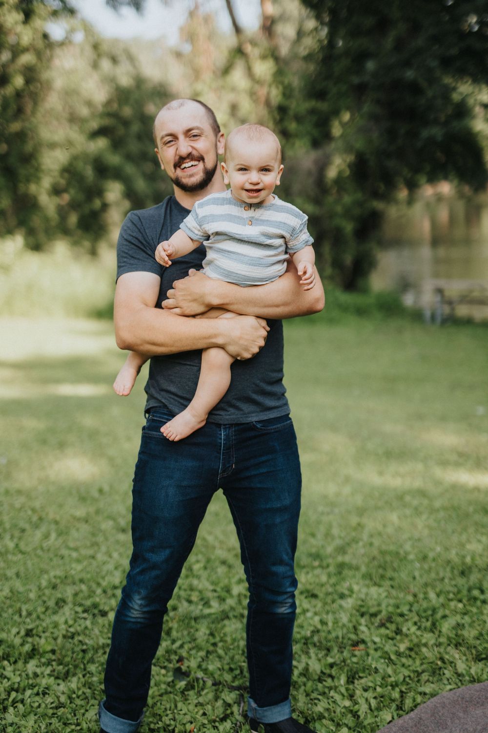 A joyful moment captured outdoors as a parent holds a smiling baby in a casual setting with greenery in the background.