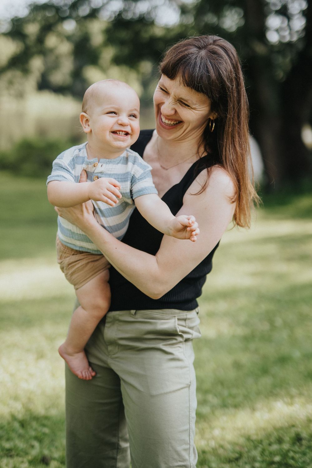 A parent and baby share joyful moments together outdoors in a grassy field on a sunny day.