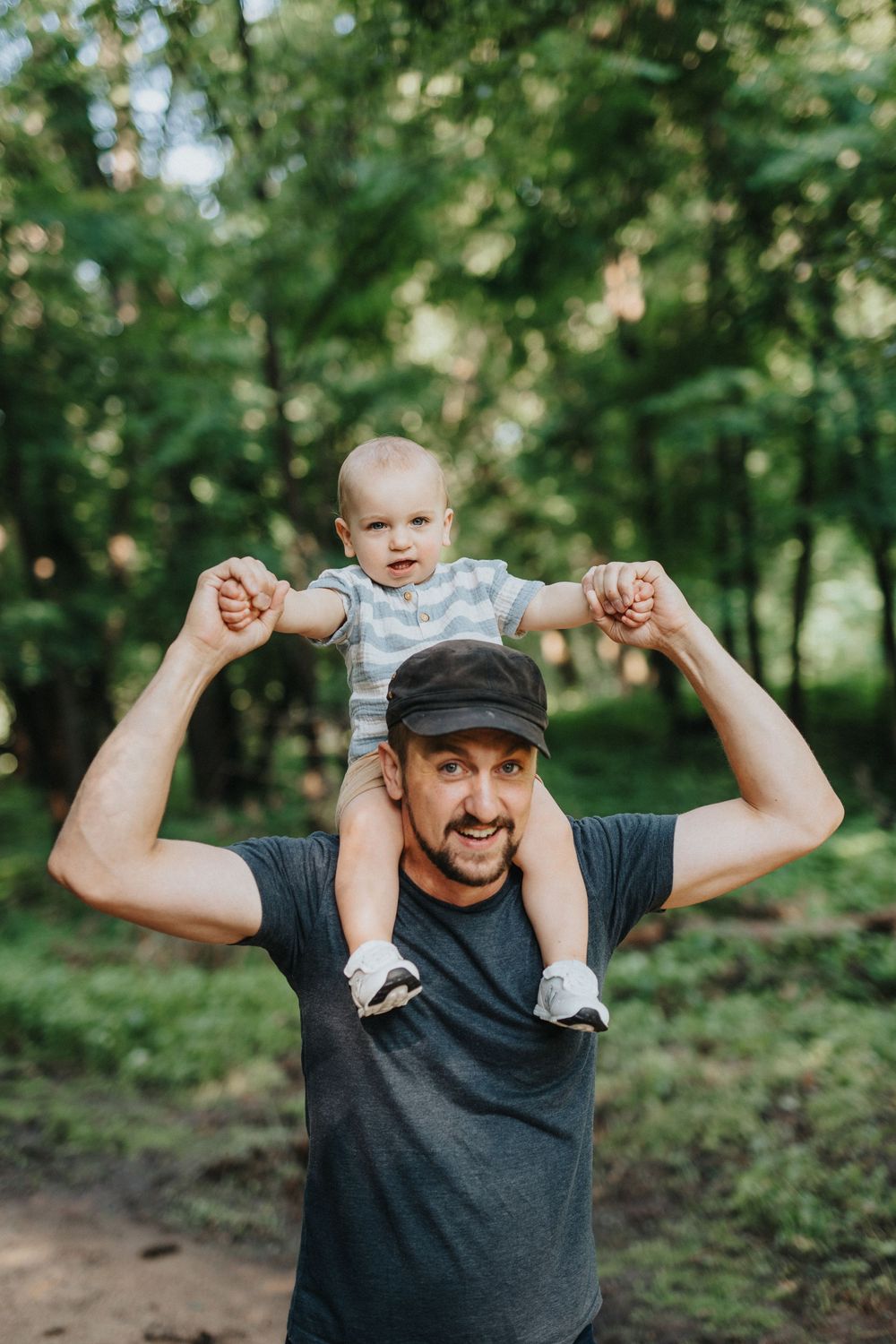 A joyful outdoor family moment with a baby riding on shoulders in a wooded setting.