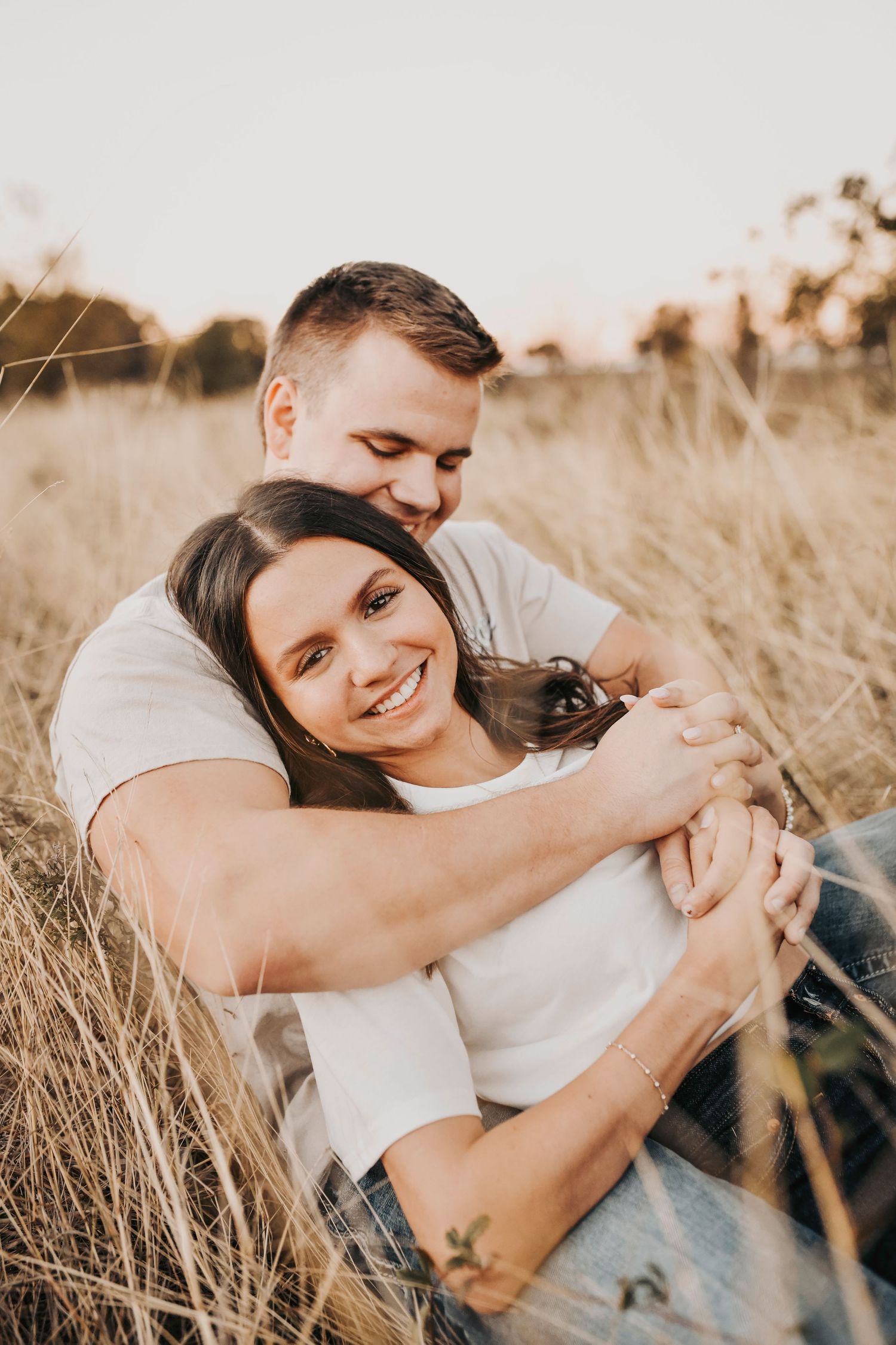 Engaged couple photographed during sunset in a rustic field with golden hour light