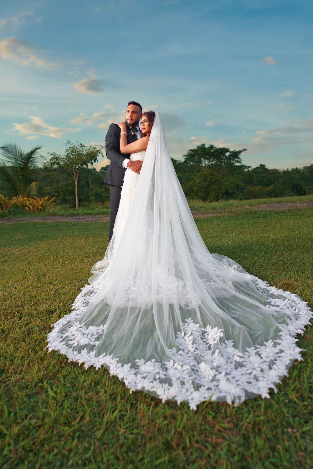 A stunning wedding dress train with intricate lace details spreads across a grassy field at sunset.