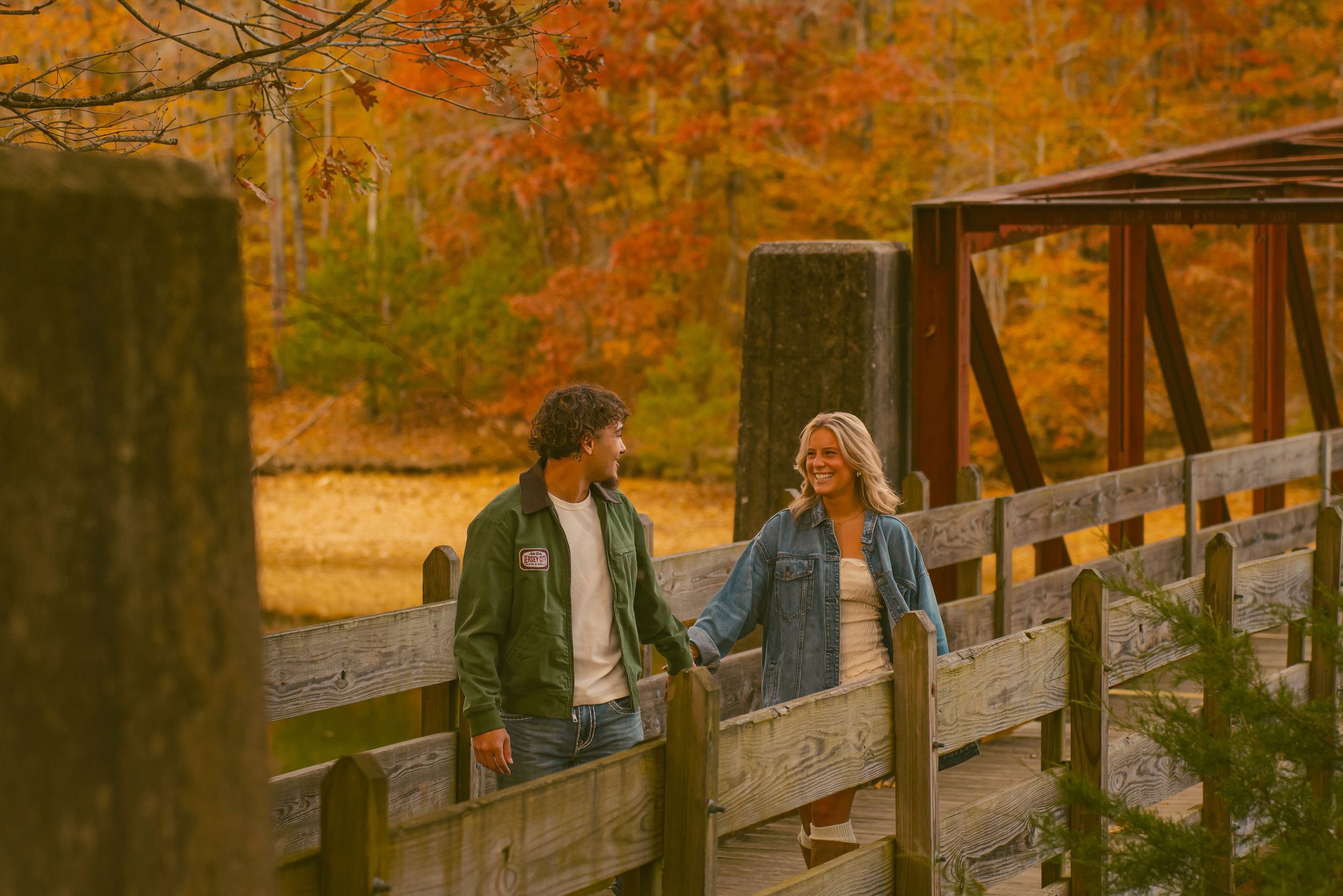 Couple walking across a wooden bridge surrounded by vibrant fall foliage and autumn colors in a park setting.