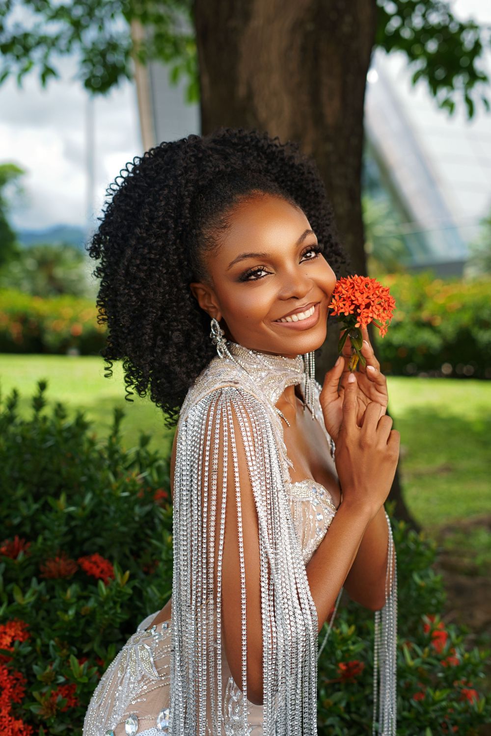 A portrait in a garden setting showing curly hair and a white lace dress while holding an orange flower.