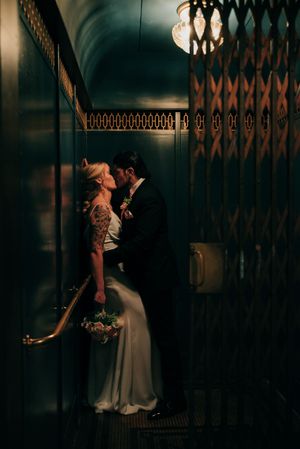 A romantic couple shares an intimate moment in a vintage elevator with ornate metalwork details at Nazareth Hall.