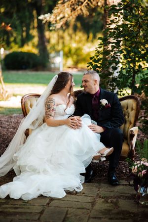 A romantic wedding couple relaxes on a vintage sofa outdoors during their garden photo session at Bloom&Bower in Risingsun, Ohio.