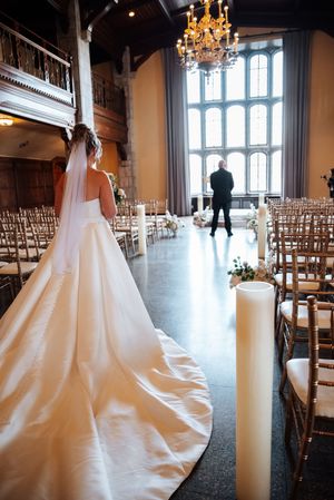 A wedding dress with a long train in an elegant venue with tall windows, chandelier and gold chiavari chairs.