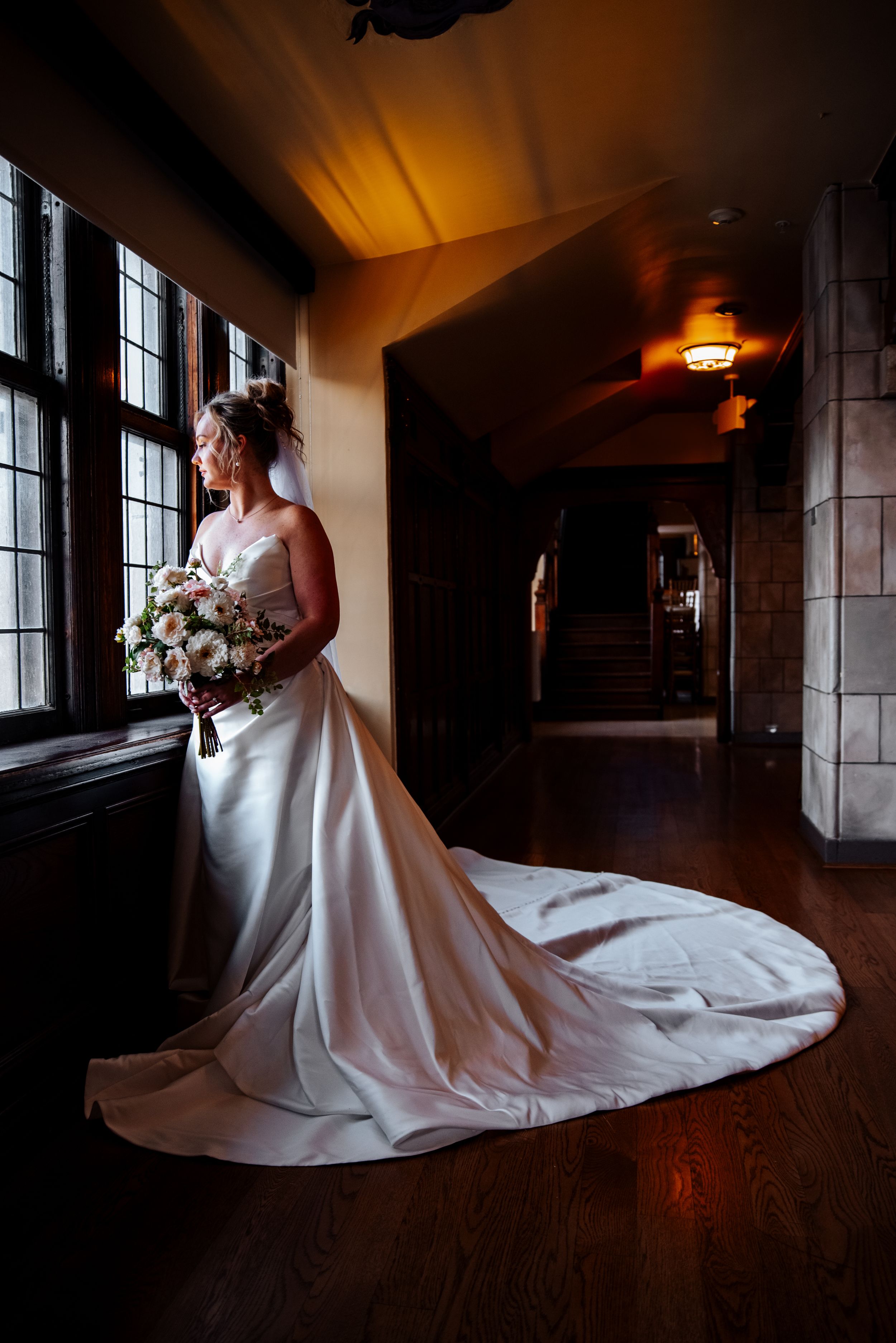 A dramatic bridal portrait series showing a flowing white wedding gown with a long train in a dark hallway.