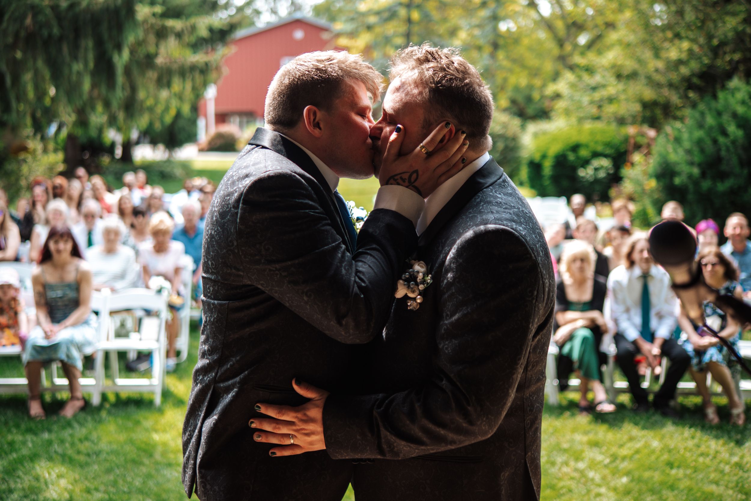 Gay Couple share a romantic kiss in a garden setting while guests look on during an outdoor celebration at Bloom&Bower in Northwest, Ohio.