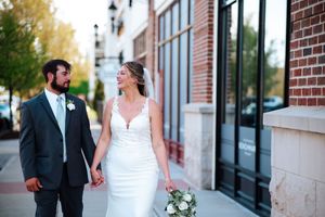 A wedding couple shares a joyful moment together while walking along a brick building exterior.
