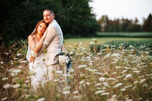 Romantic couple embraces in a dreamy summer meadow filled with delicate white wildflowers at golden hour.