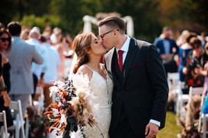A wedding couple shares a romantic kiss during an outdoor ceremony surrounded by guests and natural sunlight at the Stables in Whitehouse.