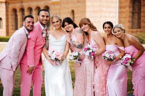Wedding party in pink dresses poses together in a row against brick wall backdrop at Nazareth Hall.