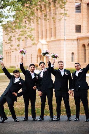 Groomsmen in black tuxedos perform playful falling domino effect pose outside historic brick building at Nazareth Hall in Grand Rapids, Ohio