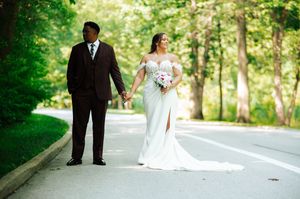 A couple in wedding attire walks along a tree-lined path on their special day in Toledo, Ohio.