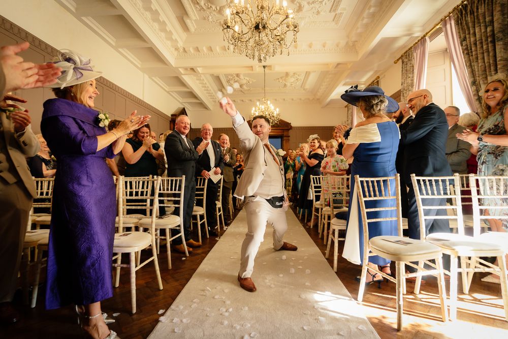 Celebratory moment at an elegant wedding reception with guests cheering in a chandelier-lit venue.