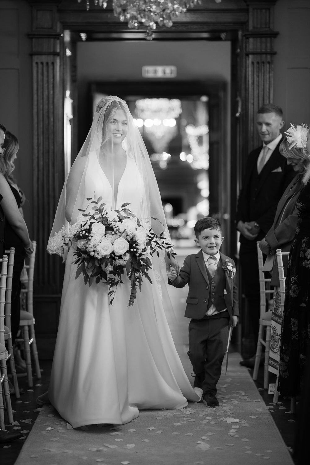 Classic black and white wedding processional in an elegant venue with ornate doorways.
