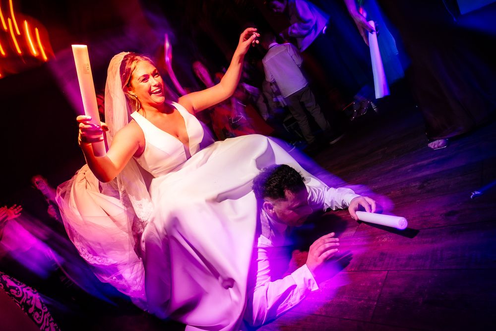 Dynamic dance floor moment with flowing white dress under vibrant purple lighting.