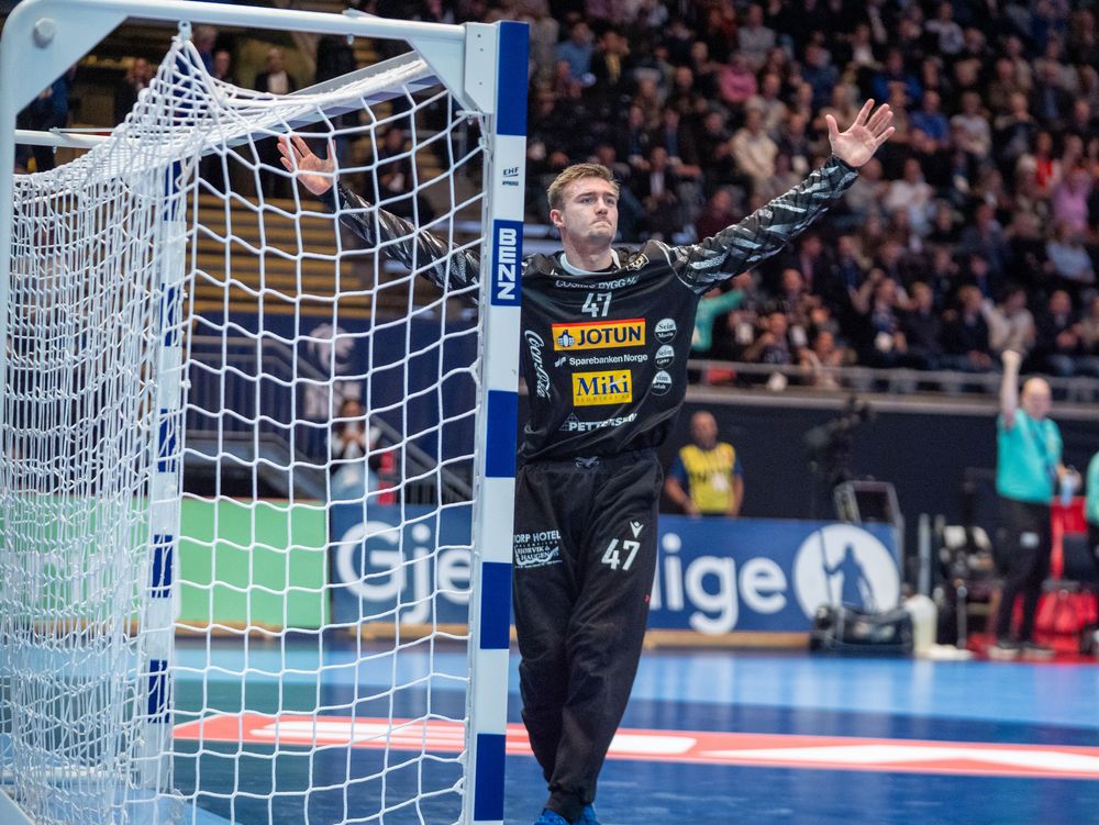 Indoor handball match with players competing near the goal during an intense game moment.