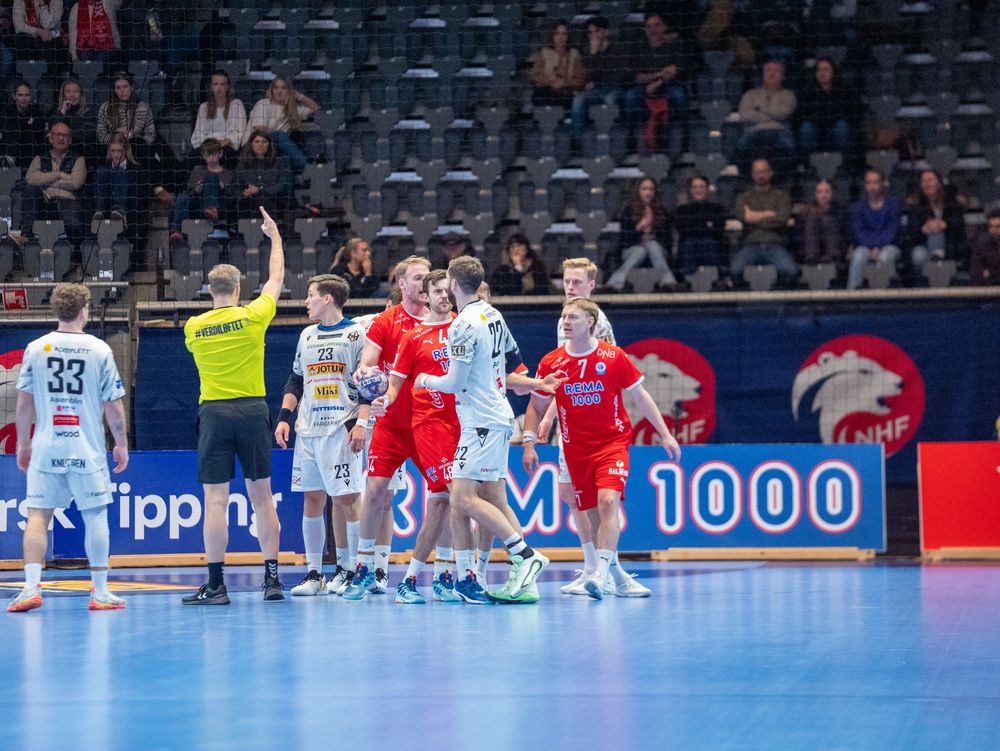 Wide view of a professional handball arena with teams in red and blue uniforms during gameplay.