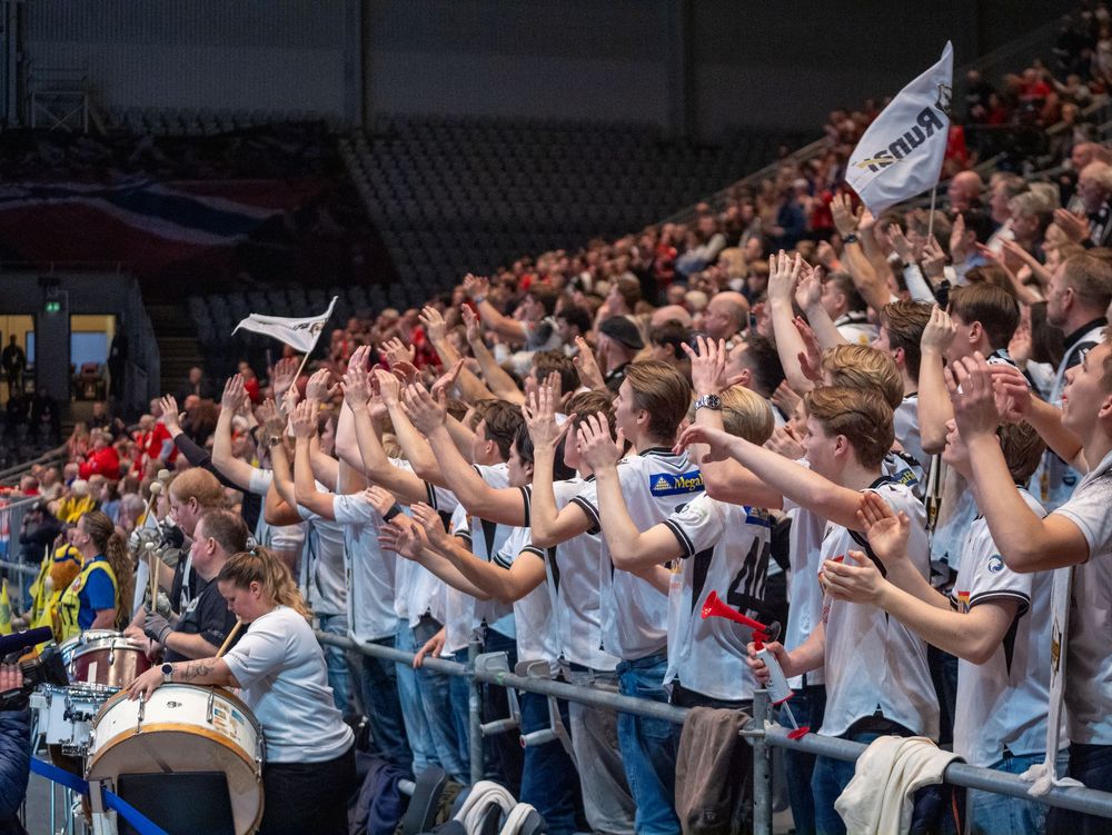 Enthusiastic sports fans in stadium seating raise their arms in synchronized celebration during a match.