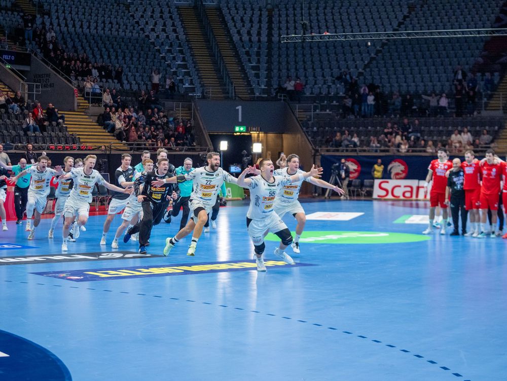 Professional handball match in progress on bright blue indoor court with players and officials.