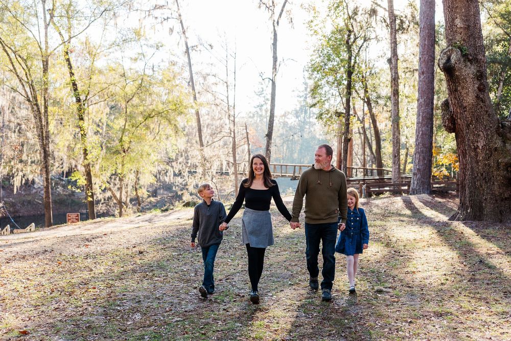 A couple walks hand in hand through a sunlit autumn forest path during a fall photoshoot session.