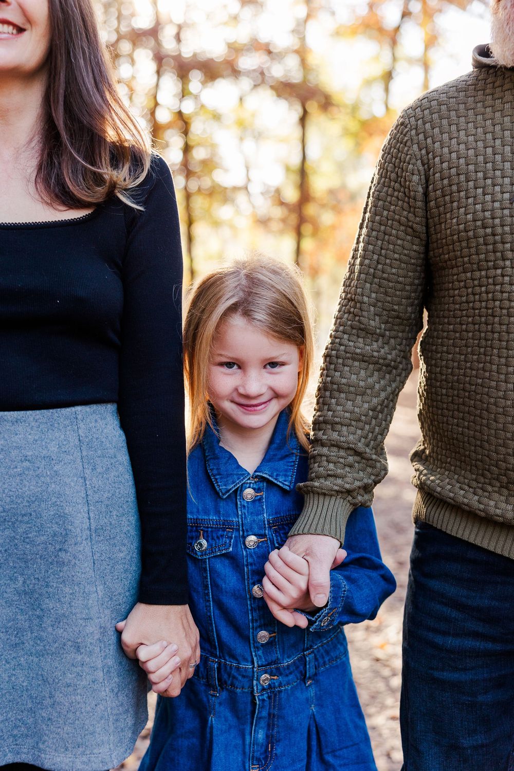 A family holds hands together while wearing denim and sweaters during an outdoor autumn photoshoot.