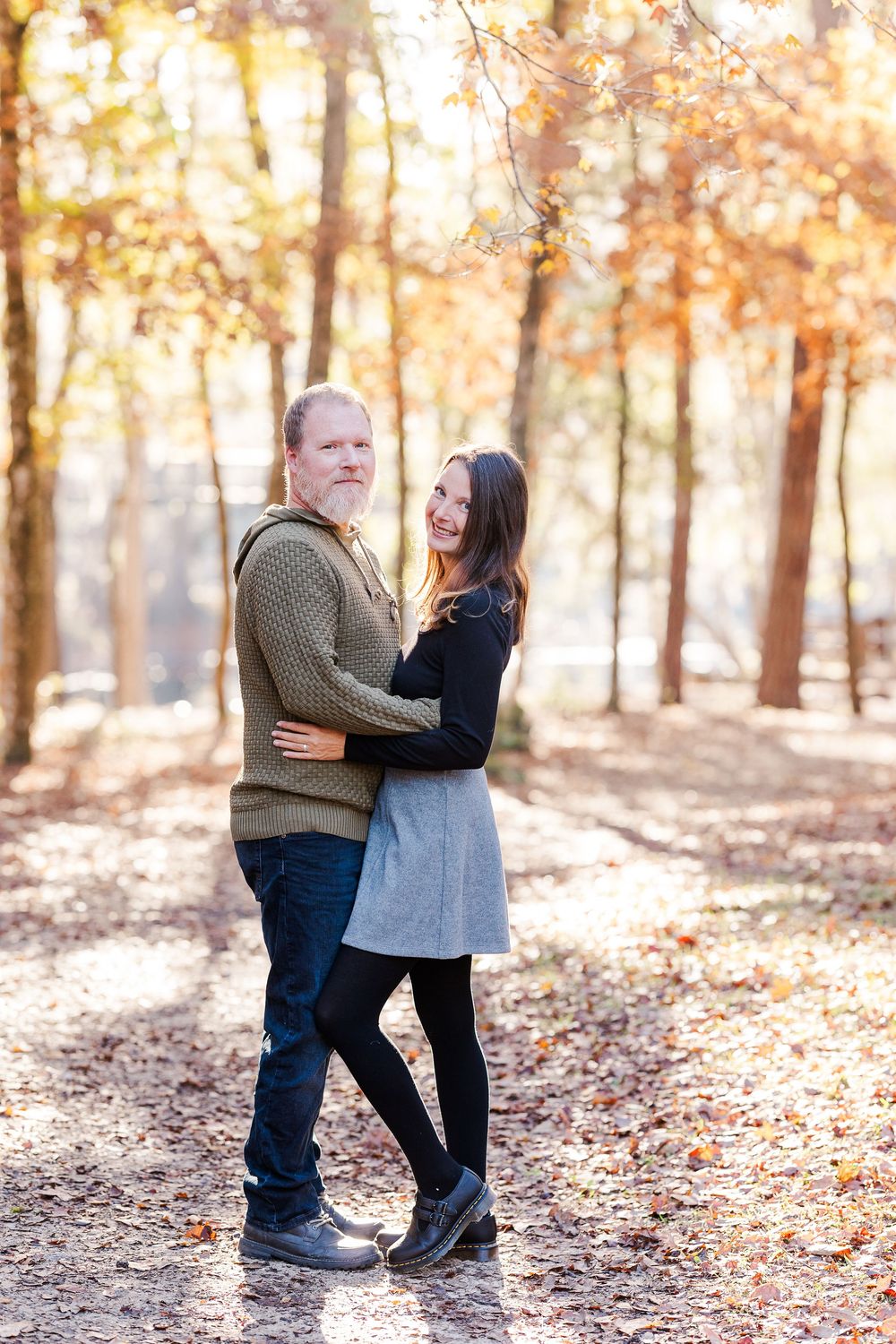 Couple embracing in romantic moment among autumn trees with golden sunlight filtering through.