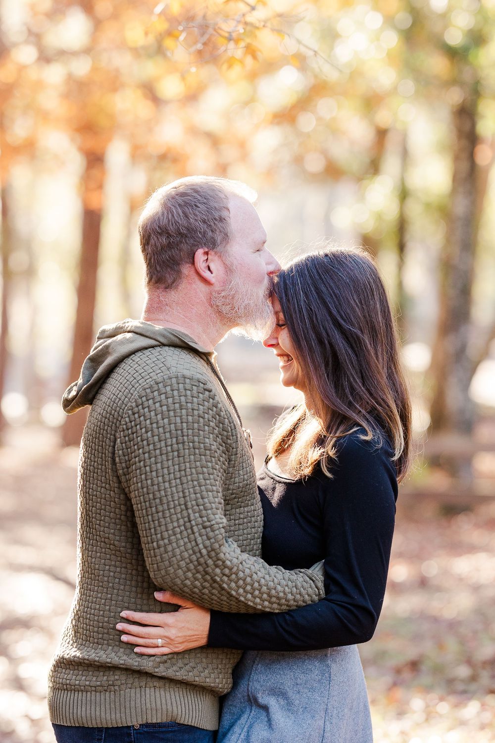 Intimate couple sharing tender moment while standing among fall foliage in forest setting.