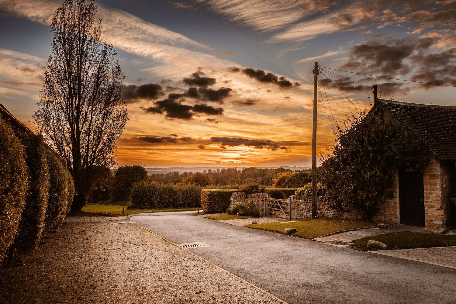 A dramatic sunset illuminates a winding country road with golden light and dramatic clouds in the rural countryside.