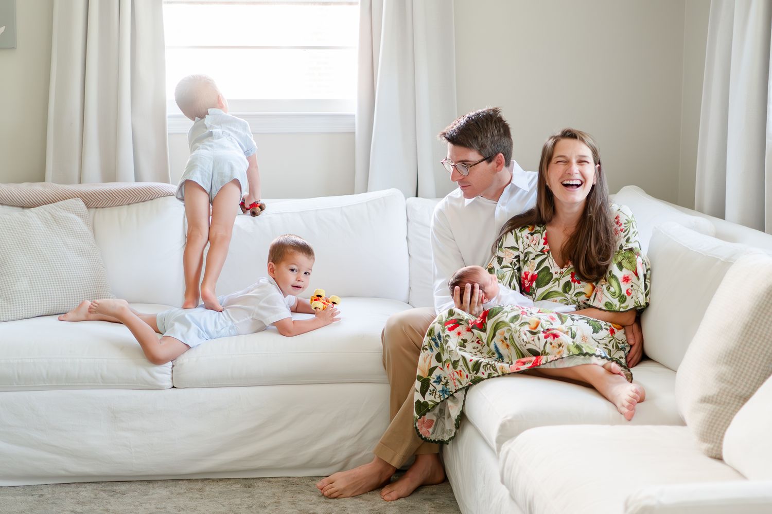 Family relaxes together on white sectional sofa in bright living room with natural light.
