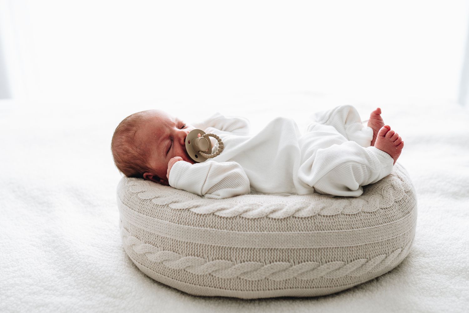 A sleeping baby lies on a cozy cable knit pillow in a bright, airy setting taken by Melbourne in-home newborn photographer.