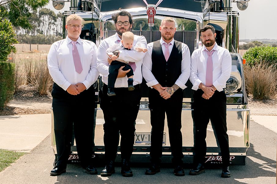 A group wearing formal black and white attire poses together outdoors on a sunny day.
