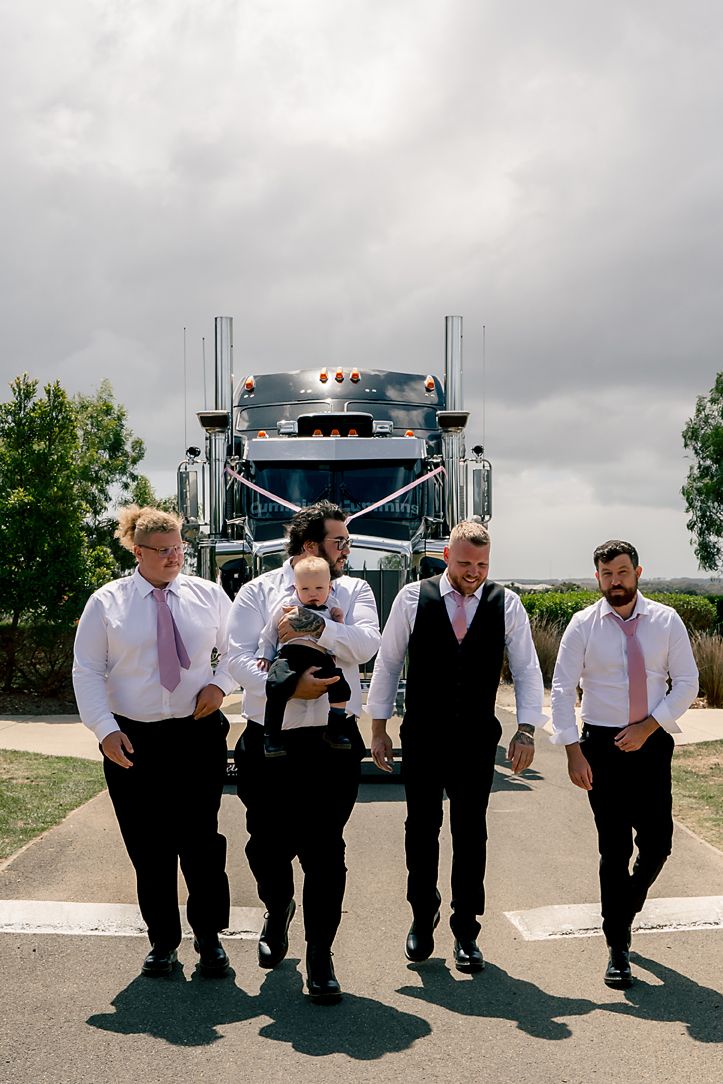 A group of formally dressed men walking together on a paved path with a large truck visible in the background.