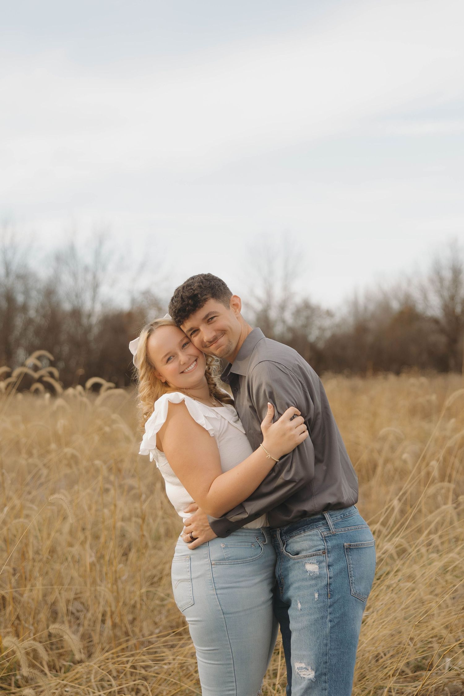 A couple embraces lovingly while standing in a golden autumn field during sunset.