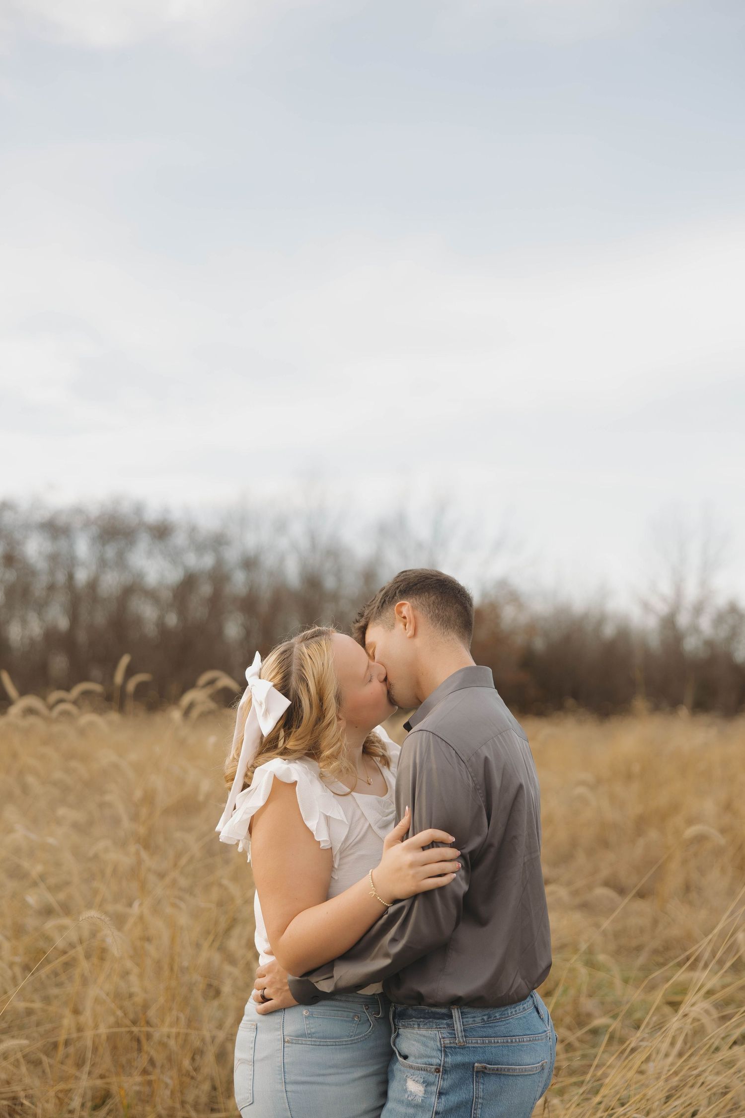 A romantic couple embraces in a golden field of tall grass during sunset.