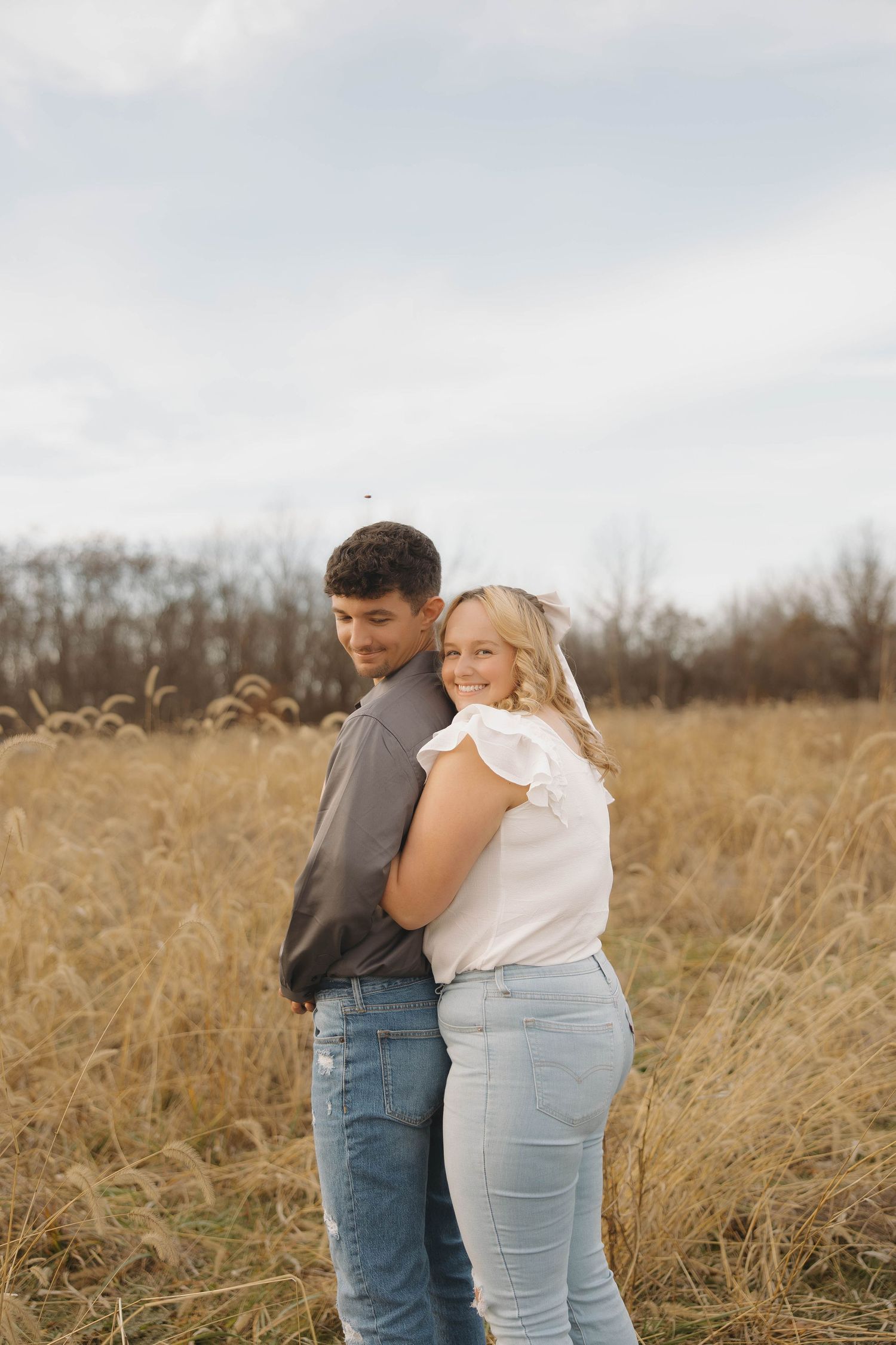 A couple embraces tenderly in a golden autumn field with tall grass swaying in the breeze.