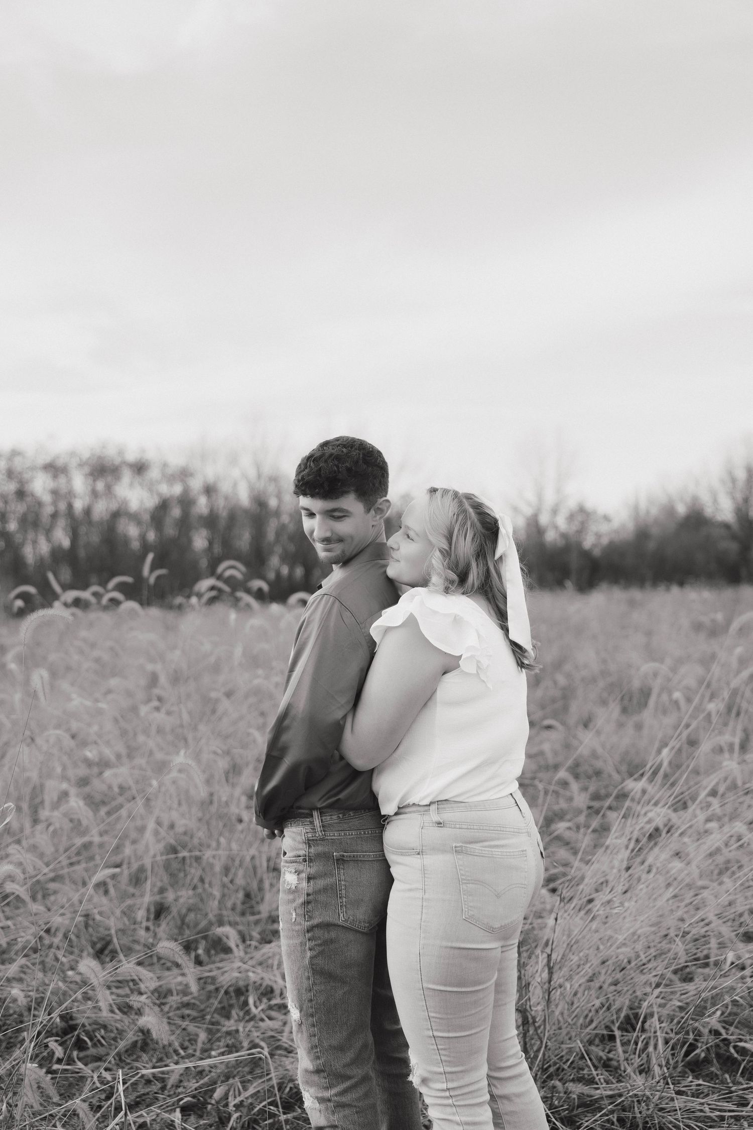 A couple embraces in a serene field of tall grass during a black and white photo session.