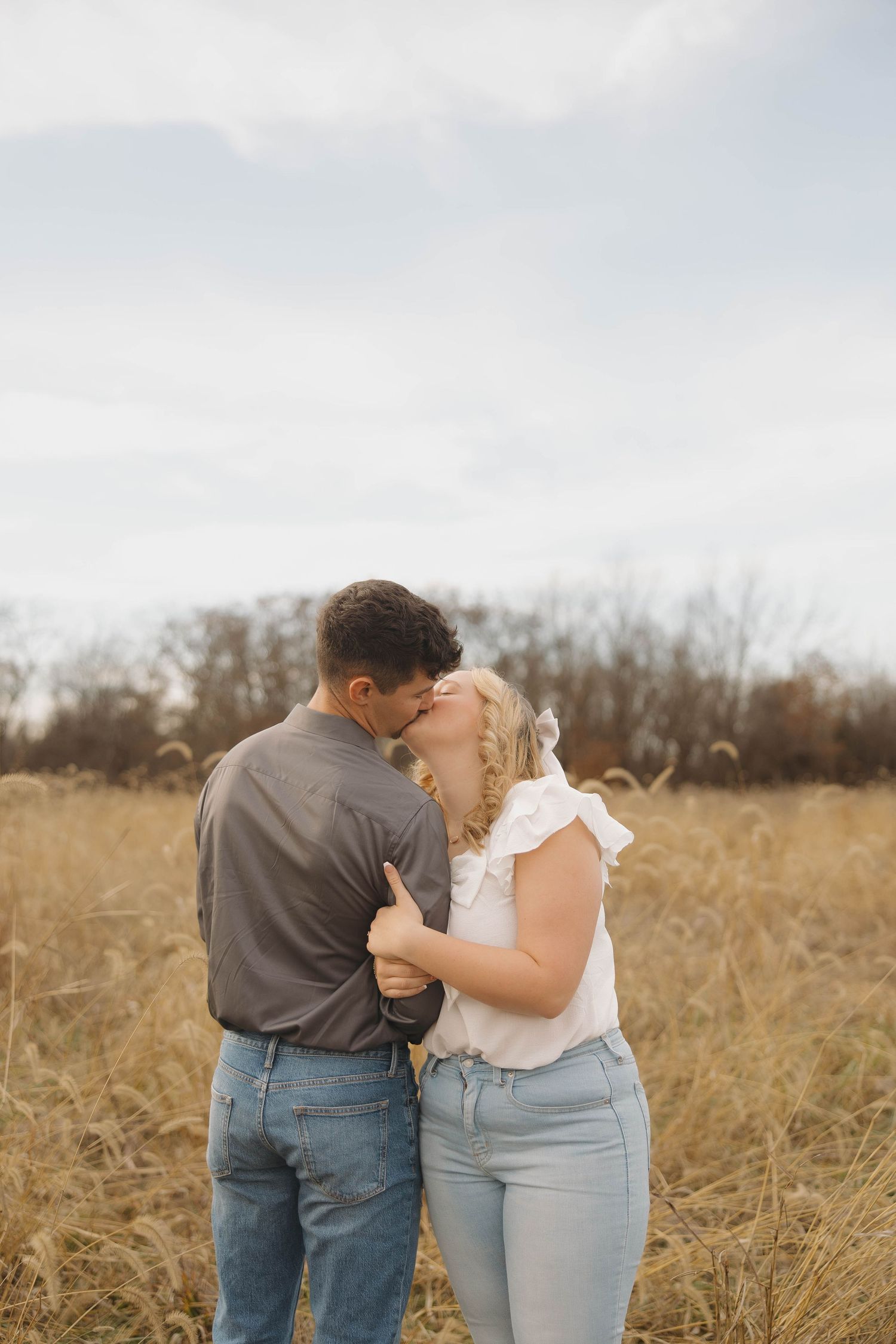 A couple shares an intimate moment together while standing in a rustic field of dried grass.