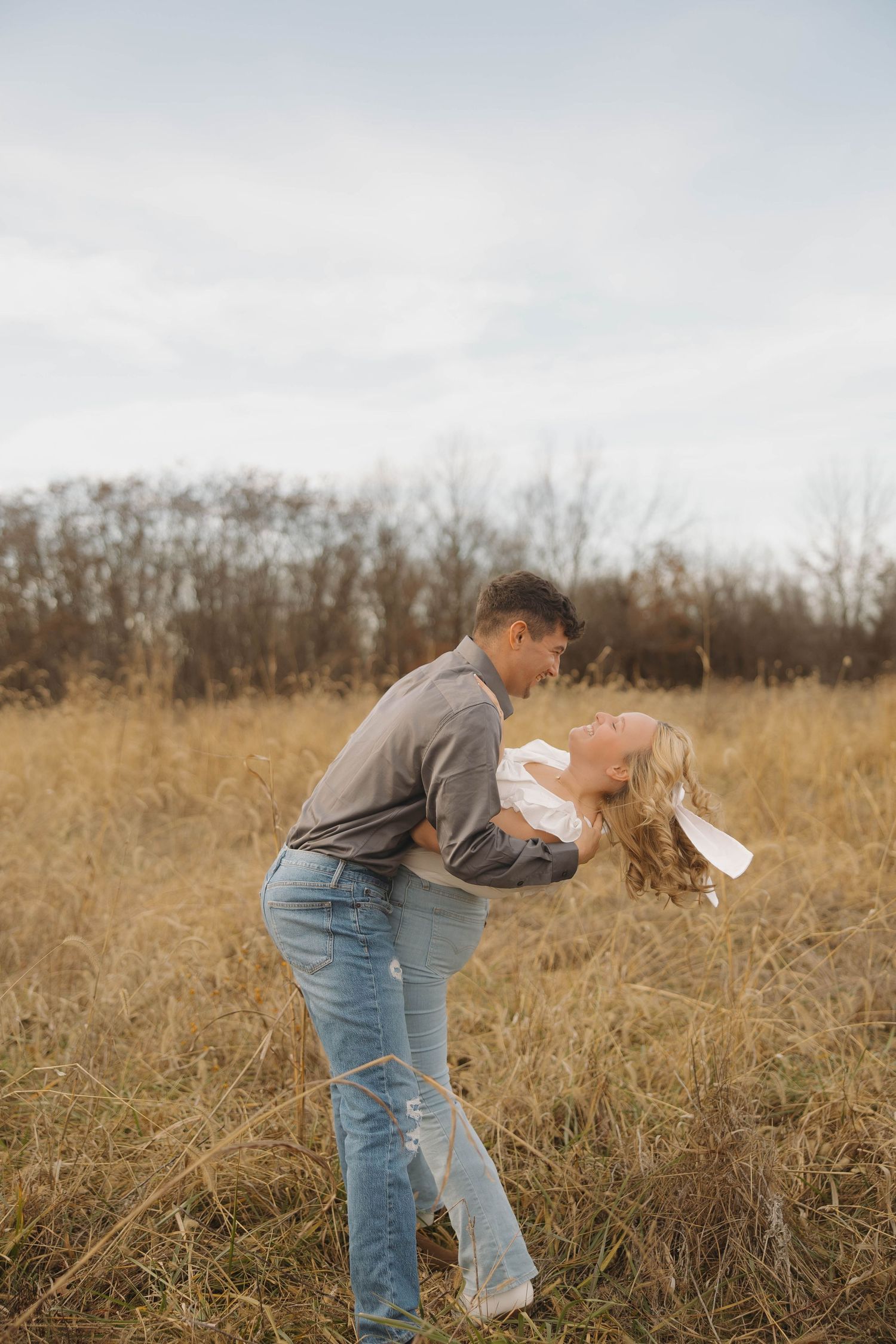 Person in denim jeans bending down to pick up trash in a golden autumn field with dried grass and bare trees.