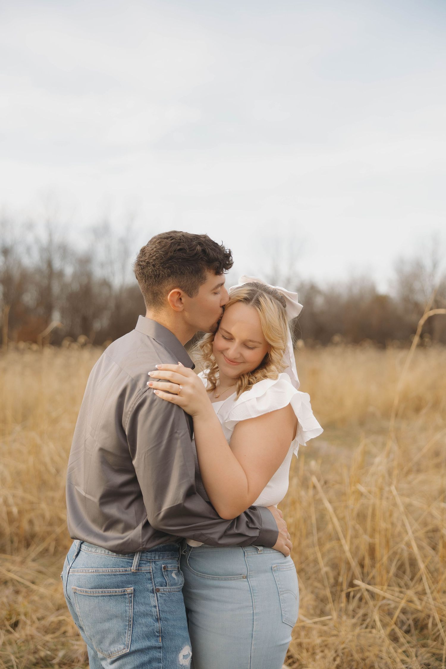 Romantic couple embracing in golden autumn field wearing casual denim and neutral colors at sunset.