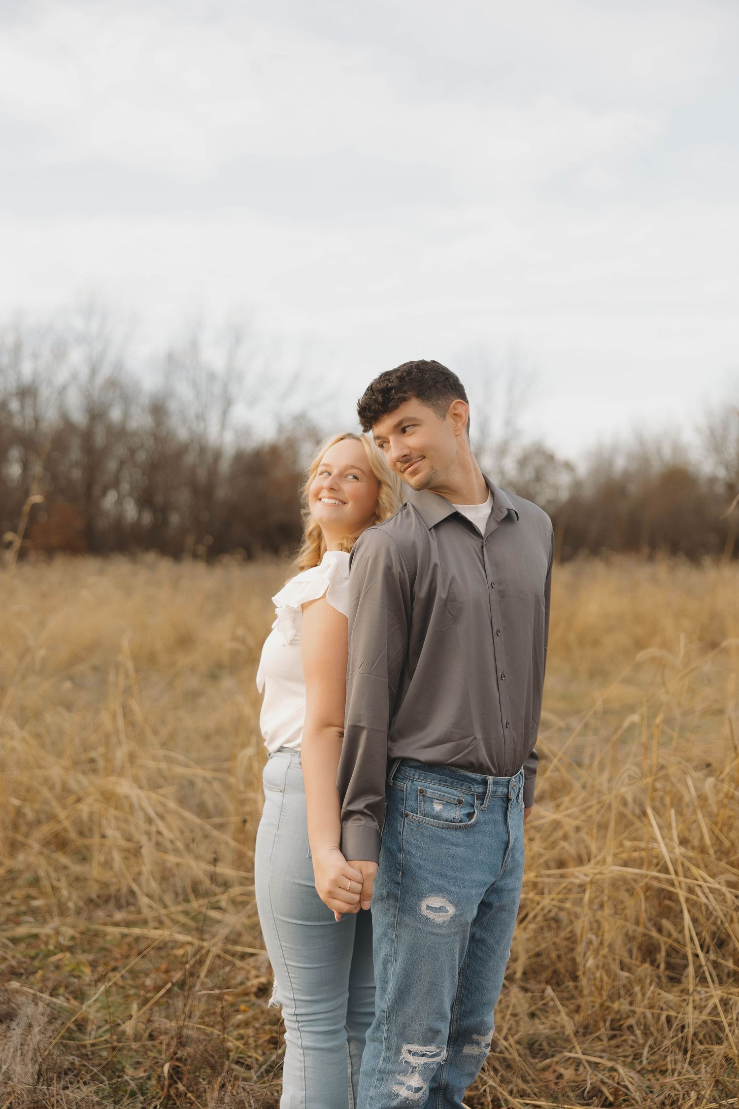A couple stands close together in a golden autumn field during sunset.